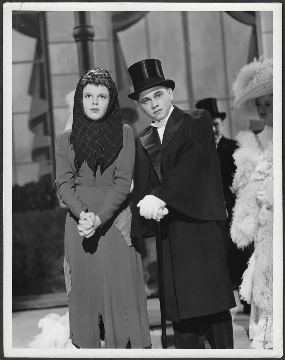 Mickey Rooney in a top hat beside Judy Garland in period costume