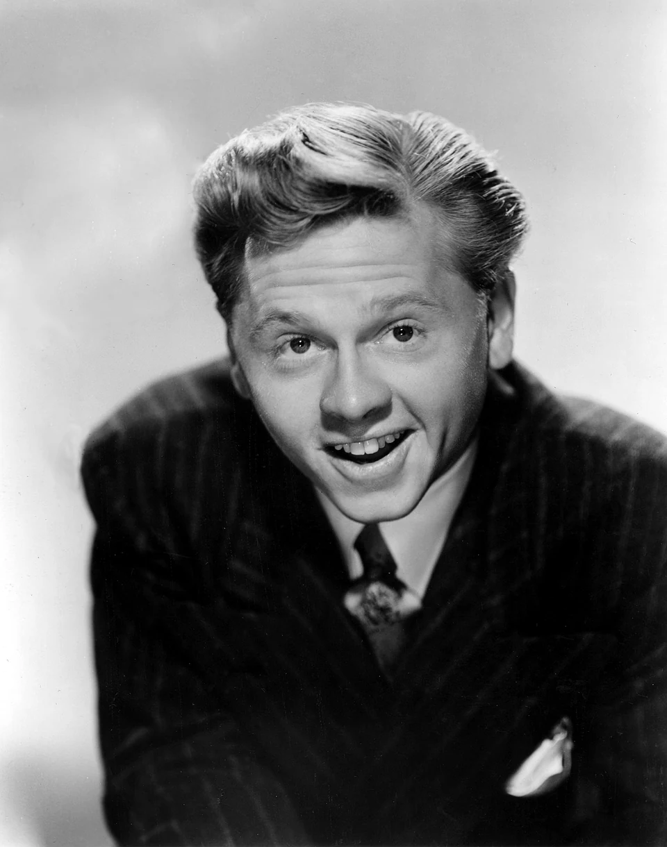 Young Mickey Rooney smiling, leaning forward in a dark suit