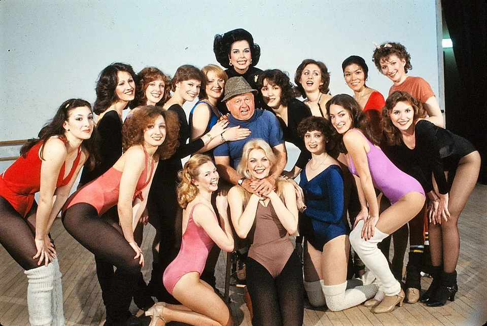 Mickey Rooney wearing a blue shirt and gray hat, surrounded by the Sugar Babies cast