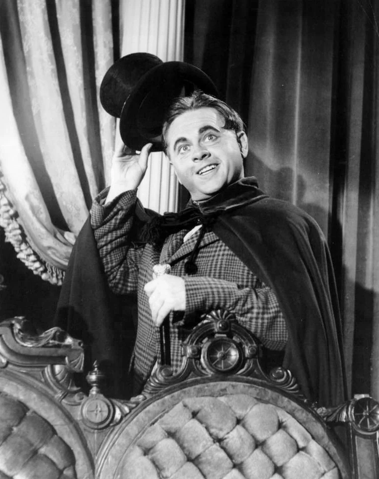 Mickey Rooney in a cape, lifting his top hat, in an NBC television publicity photograph